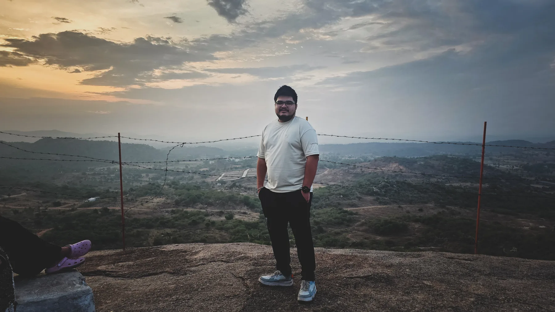 Shubhankar at a hilltop viewpoint beneath a wide, cloud-filled sky